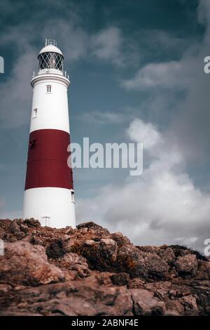 Tranquil scene of a large white and red lighthouse on a clear blue sky day surrounded by white clouds in England Stock Photo