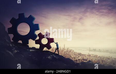 Surreal scene determined businessman pushing big cog wheels uphill. Business concept, hard working for purpose fulfilling and success achievement. Cli Stock Photo
