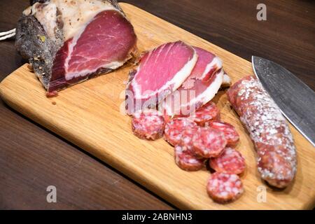 Slices of raw salted homemade ham or prosciutto and sausage on a wooden board with knife Stock Photo