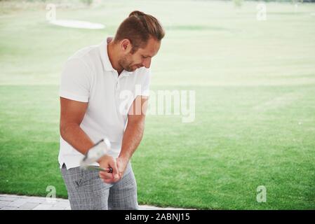 Pro golf player aiming shot with club on course. Male golfer on putting green about to take the shot, rear view Stock Photo