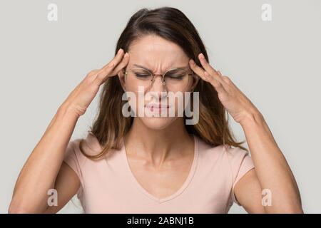 Unhappy woman wearing glasses touching temples, relieving headache Stock Photo