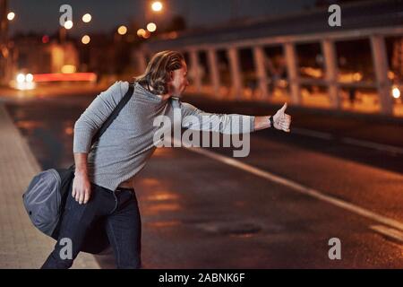Some kind of car goes along the way. Young man with bag trying to stop the car because he's late Stock Photo