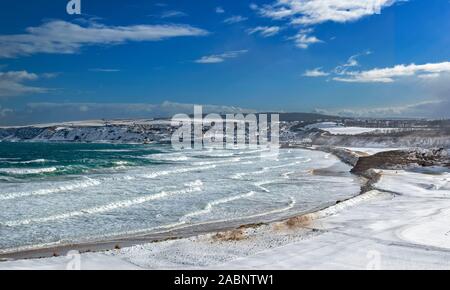 CULLEN TOWN AND CULLEN BAY MORAY COAST SCOTLAND SNOW COVERED BEACH AND WAVES ON A WINTER SEA Stock Photo