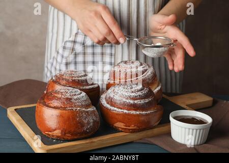 Baker holding strainer with powdered sugar over cinnamon rolls on board, closeup Stock Photo