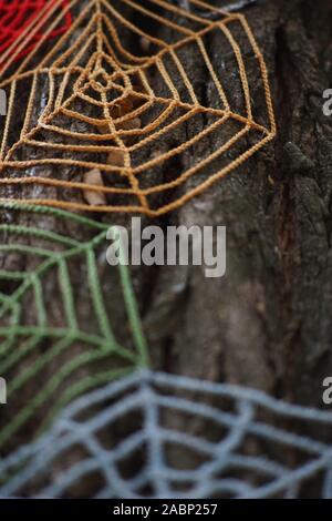 Knitted cobweb of colored threads on a tree trunk close-up. Stock Photo