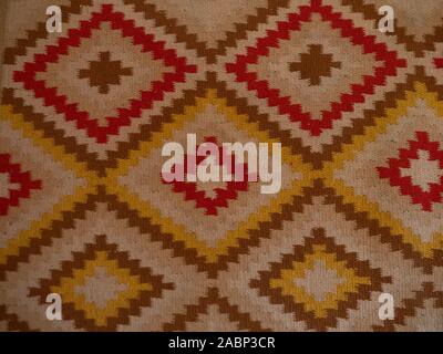 Close up of a kilim rug with tan background and zigzag diamond shapes with red, ecru, gold, and brown. Stock Photo
