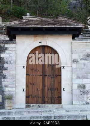 White and gray stone wall with wooden arched double door entry and slate roof. Stock Photo