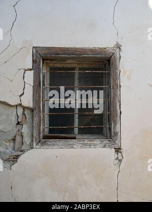 Weathered wood trim around a window with rusted metal security bars set in a crumbling and cracked stucco wall. Stock Photo