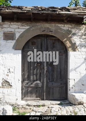 Old weathered wooden double door under a semicircular arch in a whitewashed stone wall with a slate roof overhead. Stock Photo