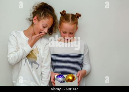 Two Surprised young teenage girl with hair bun over white background. Child holding baubles decoration for christmas tree. Stock Photo