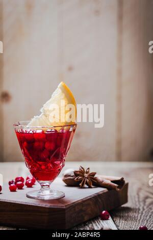 Vintage glass of mulled wine with cranberries, orange slices and star anise on rustic wooden table, close up Stock Photo