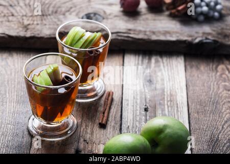 Christmas traditional winter warming cocktail, mulled apple cider drink with cinnamon sticks,  beverage in rustic glasses on wooden table, close up Stock Photo