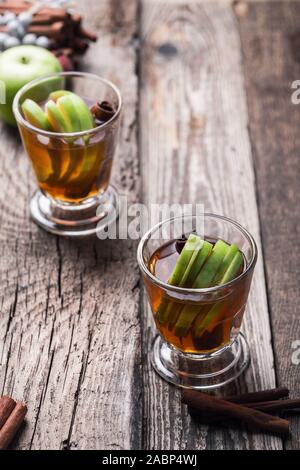 Christmas traditional winter warming cocktail, mulled apple cider drink with cinnamon sticks,  beverage in rustic glasses on wooden table, close up Stock Photo