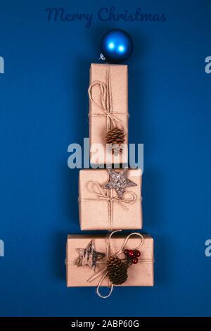 Christmas gift boxes with decoration laid out in the shape of a Christmas tree on blue background, overhead view. Stock Photo