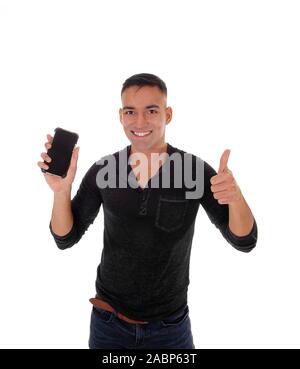 A smiling happy young man in a black shirt standing in the studio with his phone in his hand and making victory sign, isolated for white  background Stock Photo
