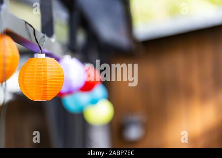 Little colorful lampion lights hanging on a pavilion in a garden on a sunny summer day. Cozy Chairs and Table standing underneath it. Stock Photo