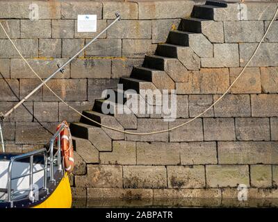 Large interlocking irregular hexagonal granite blocks forming steps in wall of Scalasaig Harbour pier, Isle of Colonsay, Scotland, UK Stock Photo