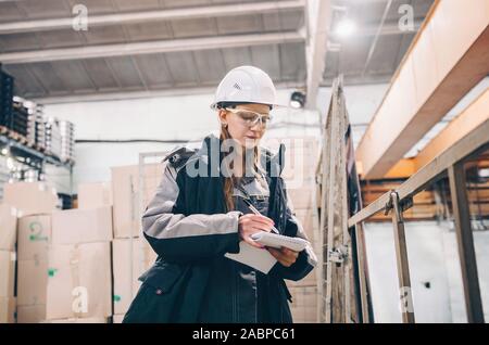 Young female technician in uniform, protective eyeglasses and helmet. Production workshop Stock Photo