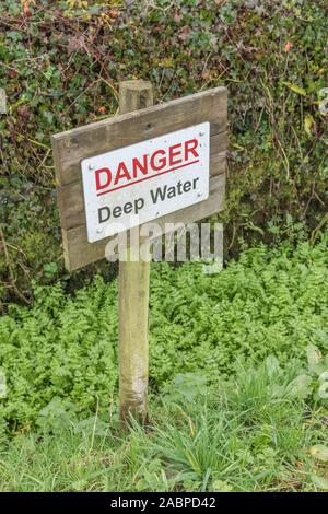 Danger warning sign for deep water drainage ditch. Plant mass may be Lesser Water-Parsnip / Berula erecta or Fool's Watercress / Apium nodiflorum. Stock Photo