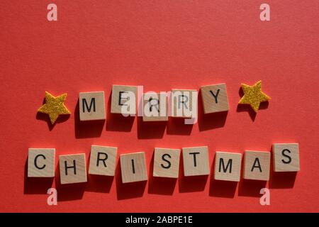 Merry Christmas in 3D wooden alphabet letters with gold glitter stars on a red background with copy space Stock Photo