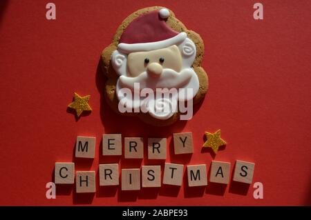 Father Christmas shaped gingerbread cookie with gold glitter stars and the message Merry Christmas, on a red background Stock Photo