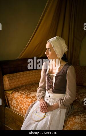 Vermeer style portrait of a young maid in renaissance costume sitting on an antique bed with her embroidery work Stock Photo