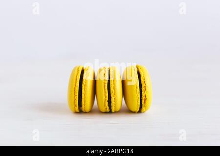 Three yellow french macarons on a wooden table. Banana macarons with chocolate cream. White background. Close-up. Stock Photo