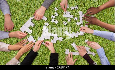 An Elevated View Group Of People Joining The White Puzzles On Green Grass Turf Stock Photo