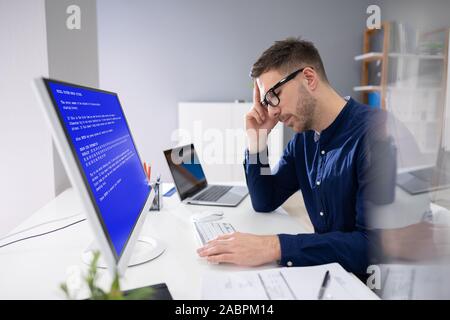 Worried Man At Computer With System Failure Screen At The Workplace Stock Photo