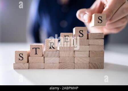 Close-up Of Person's Hand Placing Last Alphabet Of Word Stress On Wooden Block Stock Photo