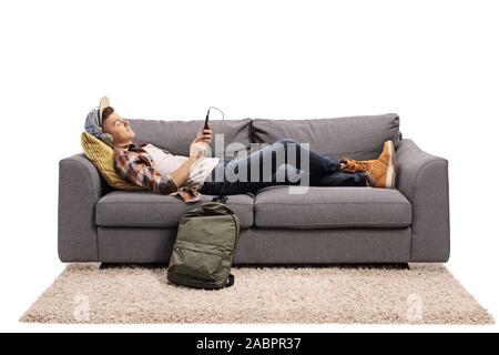 Teenage guy lying on a sofa and listening to music with headphones isolated on white background Stock Photo