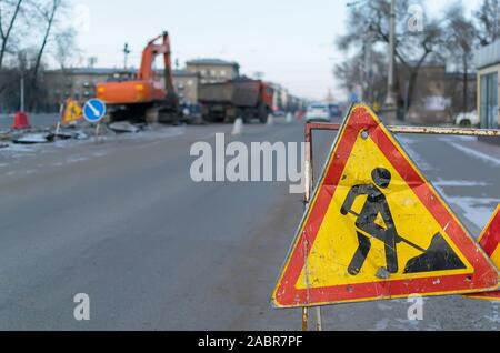 Traffic signs, detour, road repair on the background of the street and the excavator who digs the pit Stock Photo