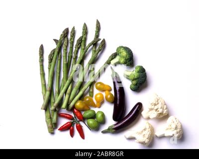 STUDIO IMAGE OF CUT VEGETABLES ON WHITE BACKGROUND (ASPARAGUS, YELLOW TOMATOES, OLIVES, CHILLIES, BROCCOLI AND CAULIFLOWER FLOWERETS. Stock Photo