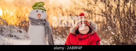 Cute boy in red winter clothes builds a snowman. Winter Fun Outdoor Concept BANNER, LONG FORMAT Stock Photo