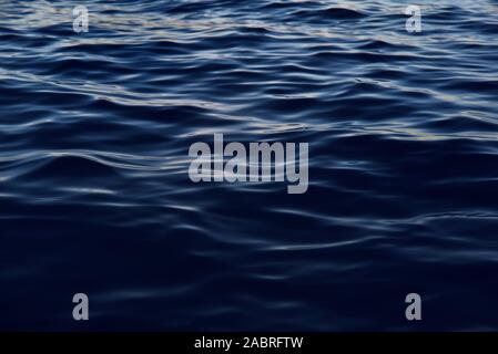 Background of dark blue gentle waves on the sea, on which the sun reflects gently Stock Photo