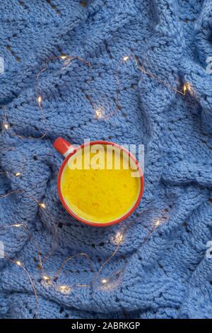 Warm and healthy anti-inflammatory drink turmeric golden milk on woolen knitted blanket with christmas lights Stock Photo