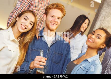 Young men and women having fun together indoors standing looking camera drinking beer hugging smiling cheerful Stock Photo