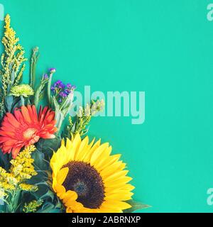 Corner border of different fresh bright colorful summer flowers lying on trendy mint background. Flat lay style. Copy space. Stock Photo