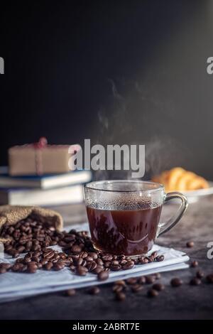 a cup of hot espresso coffee drink with smoke and roasted coffee beans on the table in the morning. vertical image, cropped shot