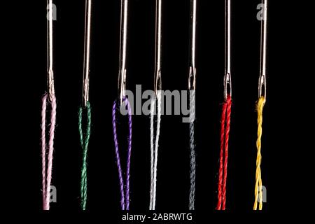 7 steel sewing needles threaded with various colored threads ready to be used in a craft project.  High Contrast and strong highlights in the steel. Stock Photo