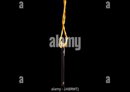A single Steel sewing needle threaded with a vivid yellow thread  on a black background ready to be used in crafts and garment repair.  There is plent Stock Photo