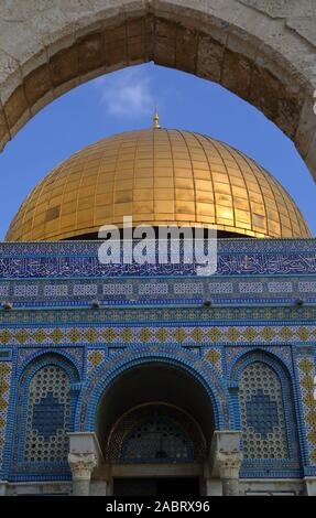 Decorative golden cupola of Dome of the rock, islamic holy place in Jerusalem, in arch of stony gate against blue sky. Stock Photo