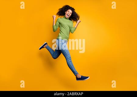 Turned full length body size photo of cheerful positive emotional curly wavy crazy fashion girl in jeans denim green sweater isolated running jumping Stock Photo