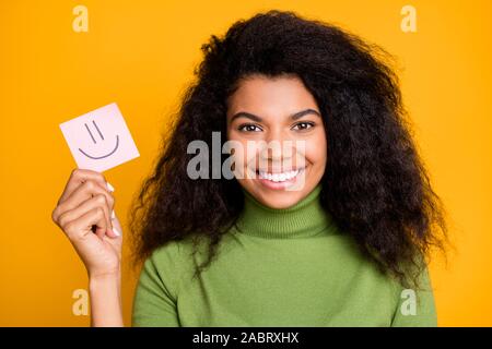 Close up photo of cheerful toothy beaming girl showing paper with emoji painted in it comparing emotions isolated vibrant color background Stock Photo