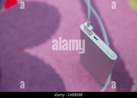 Energy bank . Smartphone Charging with silver Power Bank Through Spiral USB Cable . Smartphone charging with power bank on pink carpet . Stock Photo