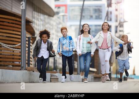 Group of multiethnic school children running together along the street after school Stock Photo