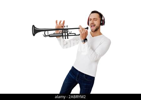 handsome young man in headphones listening to music and playing an imaginary musical trumpet isolated on white background. Stock Photo