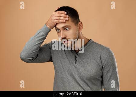 upset bearded man keeps hand on head isolated on beige background. man regrets or forget about something Stock Photo