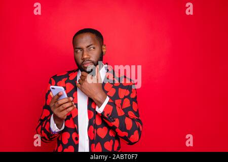Photo of funny dark skin guy holding telephone looking side unsure touch chin uncertain wear stylish hearts pattern suit blazer shirt necktie tie Stock Photo