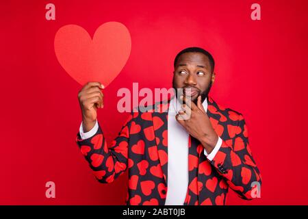 Photo of funny dark skin man cupid hold big paper heart thinking over creative way of love confession wear hearts pattern suit shirt necktie tie Stock Photo